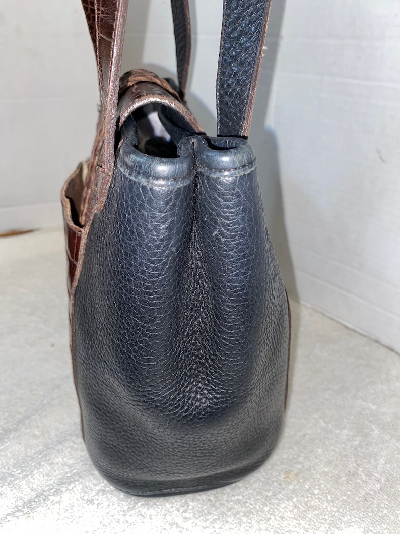 May include: A brown and black leather tote bag with a top handle and a zip closure.