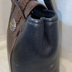 May include: A brown and black leather handbag with a silver buckle. The bag has a top handle and a shoulder strap.