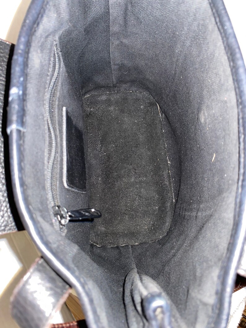 May include: The inside of a black leather tote bag with a zipped pocket and a suede lining.
