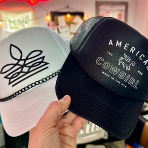 White boot stitch cowgirl trucker hat styled beside black American Cowgirl cap