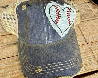 May include: A blue denim baseball cap with a distressed look. The cap has a mesh back and a white heart with a red baseball stitch design on the front.