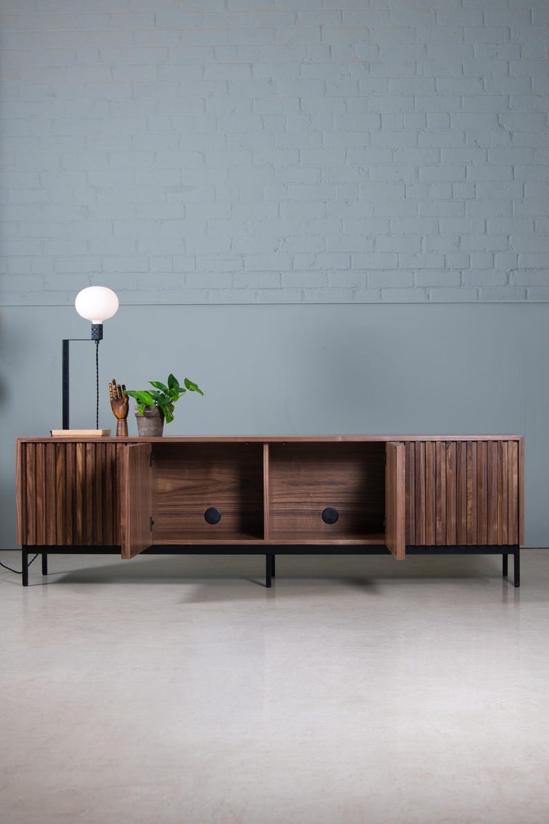 May include: A dark wood media console with three doors, two of which are open, revealing empty shelves. The console has black metal legs and is sitting on a light gray floor.