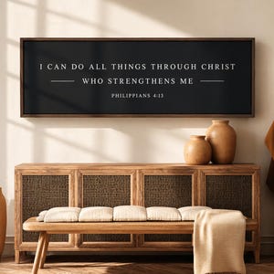 May include: A rectangular wall sign with a dark charcoal background and a thin brown frame. The white text reads: I CAN DO ALL THINGS THROUGH CHRIST WHO STRENGTHENS ME, followed by the citation PHILIPPIANS 4:13 in a clean, sans-serif font.