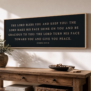 May include: A rectangular wall sign with a black background and a light wood frame. The text in gold lettering reads: THE LORD BLESS YOU AND KEEP YOU; THE LORD MAKE HIS FACE SHINE ON YOU AND BE GRACIOUS TO YOU; THE LORD TURN HIS FACE TOWARD YOU AND GIVE YOU PEACE. NUMBERS 6:24-26.