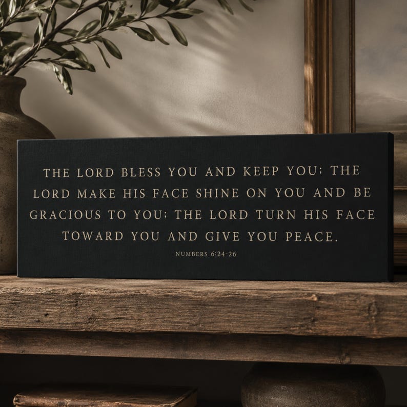 May include: A rectangular black sign featuring gold-colored text that reads: THE LORD BLESS YOU AND KEEP YOU; THE LORD MAKE HIS FACE SHINE ON YOU AND BE GRACIOUS TO YOU; THE LORD TURN HIS FACE TOWARD YOU AND GIVE YOU PEACE. NUMBERS 6:24-26.