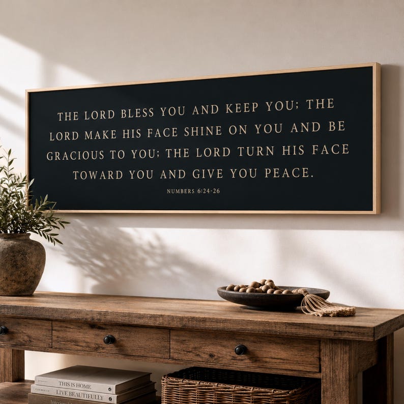 May include: A rectangular wall sign with a black background and a light wood frame. The text in gold lettering reads: THE LORD BLESS YOU AND KEEP YOU; THE LORD MAKE HIS FACE SHINE ON YOU AND BE GRACIOUS TO YOU; THE LORD TURN HIS FACE TOWARD YOU AND GIVE YOU PEACE. NUMBERS 6:24-26.