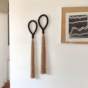 May include: Two black macrame wall hangings with long, natural fiber tassels.