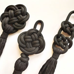 May include: Three black macrame tassel keychains with different knot patterns. Each keychain has a long tassel made of black cord.