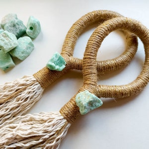 Op de afbeelding: Twee macramé wandhangers met natuurlijk jute touw en kwastjes. Elke hanger heeft een lichtgroen kristal accent.