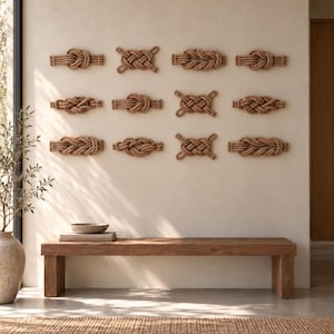 May include: A collection of twelve wall-mounted decorative rope knots arranged in a grid pattern. Each knot is crafted from thick, natural-colored twisted fiber rope, featuring distinct weaving styles and textures secured to the wall.