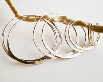 May include: Set of four silver hoop earrings of varying sizes. The hoops are smooth and have a hammered texture.