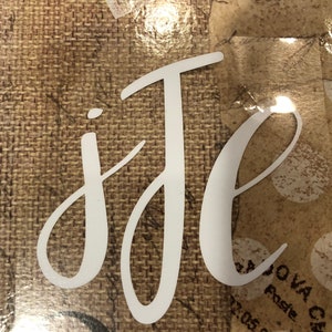 May include: White cursive lettering on a brown background that reads "j'de".