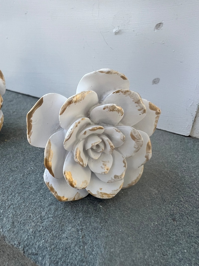 May include: White ceramic flower with gold accents. The flower has a layered, rosette design.