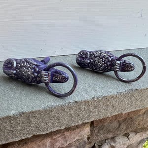May include: Two purple metal door handles with a decorative fish design and a ring pull.