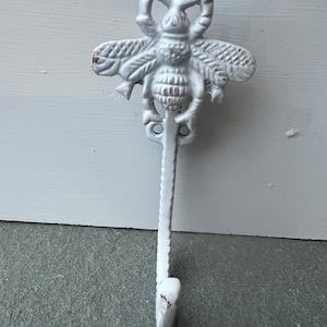 May include: White metal bee hook with a decorative bee design. The hook is attached to a metal rod that ends in a rounded point.