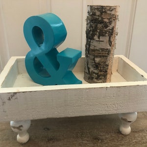 May include: White wooden tray with four legs, featuring a teal ampersand and a birch log.