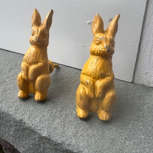May include: Two yellow ceramic rabbit figurines. The rabbits are sitting upright with their ears perked up. They have a distressed finish and would be a cute addition to a farmhouse or cottagecore decor.