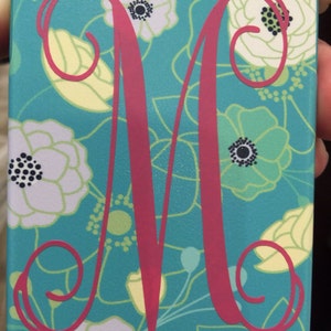 May include: A turquoise phone case with a white floral pattern and a pink letter M monogram.