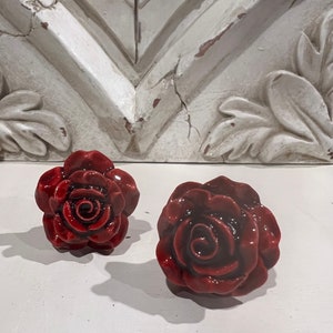 May include: Two red ceramic rose-shaped drawer pulls. The roses have a glossy finish and are detailed with a swirl in the center.