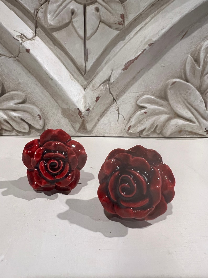 May include: Two red ceramic rose-shaped drawer pulls. The roses have a glossy finish and are detailed with a swirl in the center.