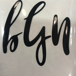 May include: Black vinyl lettering that reads "bgn" in a cursive font.