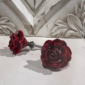 May include: Two red ceramic rose drawer pulls with a silver metal screw.