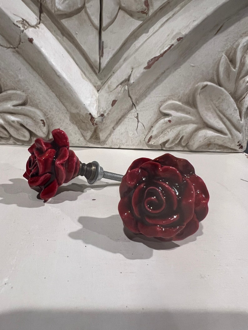 May include: Two red ceramic rose drawer pulls with a silver metal screw.