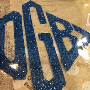 May include: Blue glitter monogram letters "OBY" in a diamond shape on a brown background.