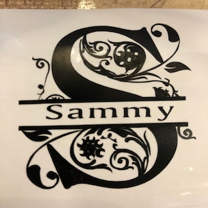 May include: Black and white vinyl decal of the letter S with ornate floral designs. The name "Sammy" is written in a banner below the letter.
