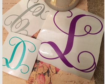 May include: Three vinyl decals with cursive letters. The letters are D, L, and a. The D is teal, the L is purple, and the a is silver.