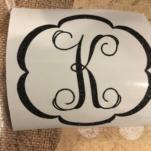 Pode incluir: Um adesivo de vinil preto com glitter com uma letra K cursiva em um círculo branco.