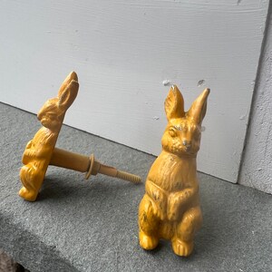 May include: Two yellow ceramic rabbit door knobs. The rabbit on the left is facing the left and the rabbit on the right is facing the right. Both rabbits have their paws crossed in front of them.