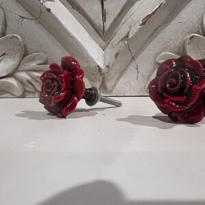 May include: Two red rose-shaped ceramic drawer pulls with silver metal stems.