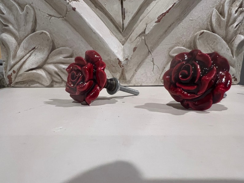 May include: Two red rose-shaped ceramic drawer pulls with silver metal stems.