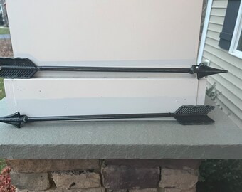 May include: Two black metal arrow wall decor pieces mounted on a white wall. The arrows are pointing to the right.