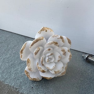 May include: White ceramic flower knob with gold accents. The flower has a detailed design and is perfect for adding a touch of elegance to any room.