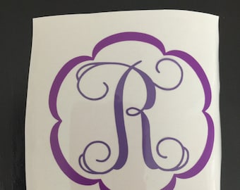 May include: A purple monogram decal featuring the letter "R" in a decorative script font. The letter is centrally positioned within a scalloped circle.