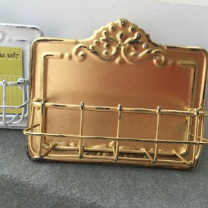 May include: Gold metal business card holder with a decorative design. The holder has a wire rack to hold cards.