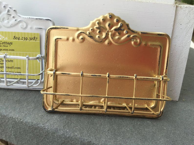 May include: Gold metal business card holder with a decorative design. The holder has a wire rack to hold cards.