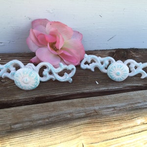 May include: Two white and turquoise decorative drawer pulls with a floral design. The pulls have a distressed finish and are perfect for adding a touch of vintage charm to any home.