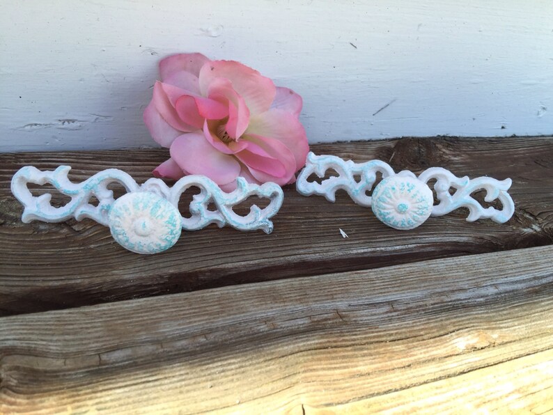 May include: Two white and turquoise decorative drawer pulls with a floral design. The pulls have a distressed finish and are perfect for adding a touch of vintage charm to any home.