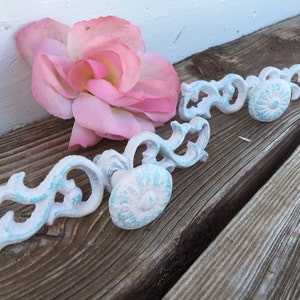 May include: Two white, ornate, decorative cabinet knobs with blue accents. The knobs have a floral design and are made of metal.