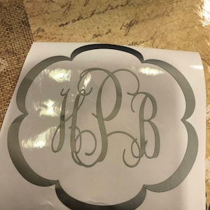 Pode incluir: Um adesivo de monograma prateado com as letras "H.P.B." em uma fonte cursiva. O adesivo está em um fundo branco e tem uma borda festoneada.