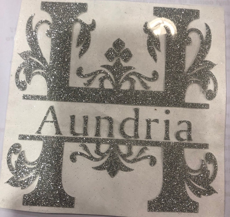 May include: Silver glitter monogram decal with the letter "H" and the name "Aundria" below. The letter "H" is decorated with ornate floral designs.