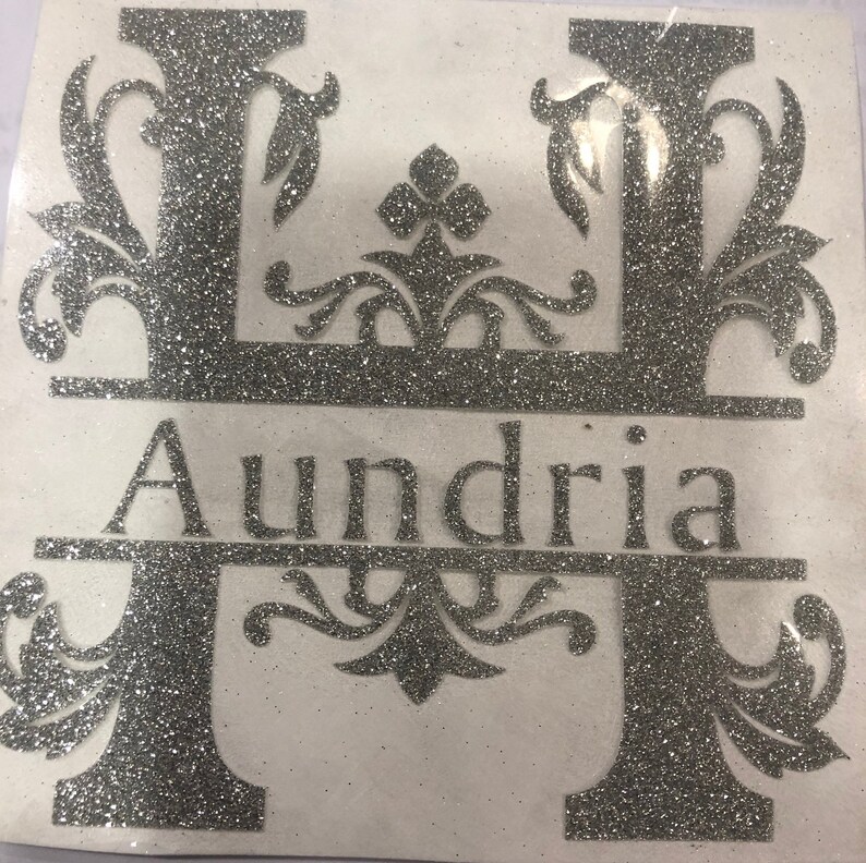 May include: A silver glitter letter H with decorative flourishes and the name "Aundria" written below it.