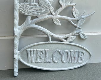 May include: White cast iron welcome sign with a bird's nest and two birds on a branch with leaves. The sign says "WELCOME" in a distressed font.