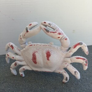 May include: A white cast iron crab figurine with red paint accents. The crab is in a standing position with its claws raised.