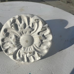 May include: White decorative knob with a raised floral design. The knob has a distressed finish with hints of gold.