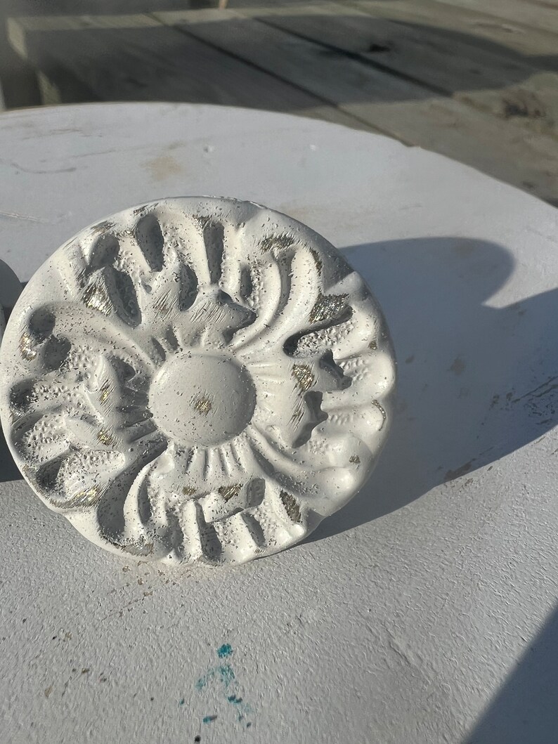 May include: White decorative knob with a raised floral design. The knob has a distressed finish with hints of gold.