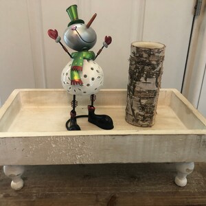 May include: White wooden tray with four legs, featuring a snowman figurine with a green scarf and red mittens, and a birch bark candle holder.